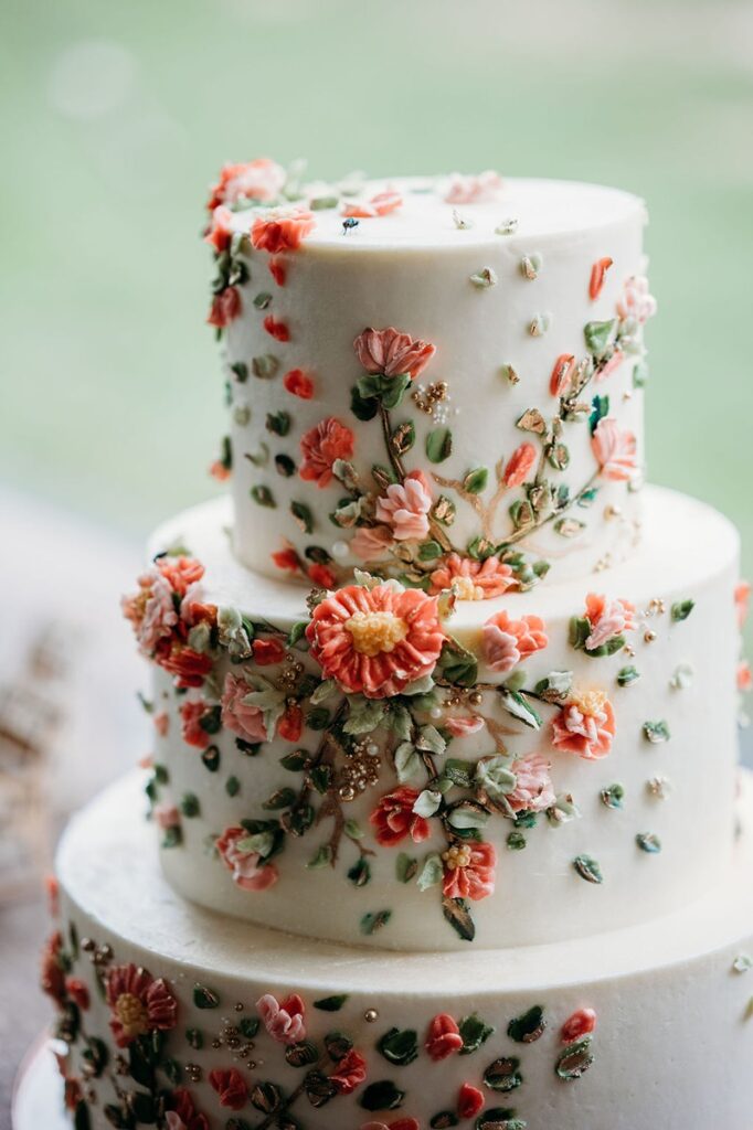 close up of wedding cake with coral florals and greenery on it