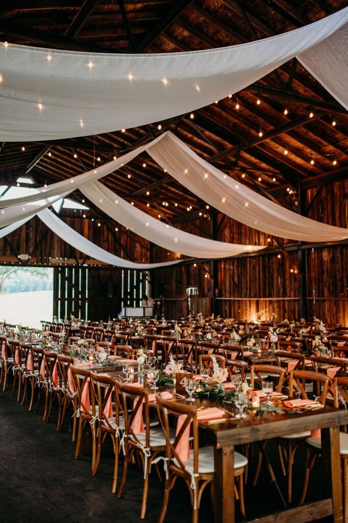 inside of a barn during a wedding reception, string lights and canopy draped from the roof
